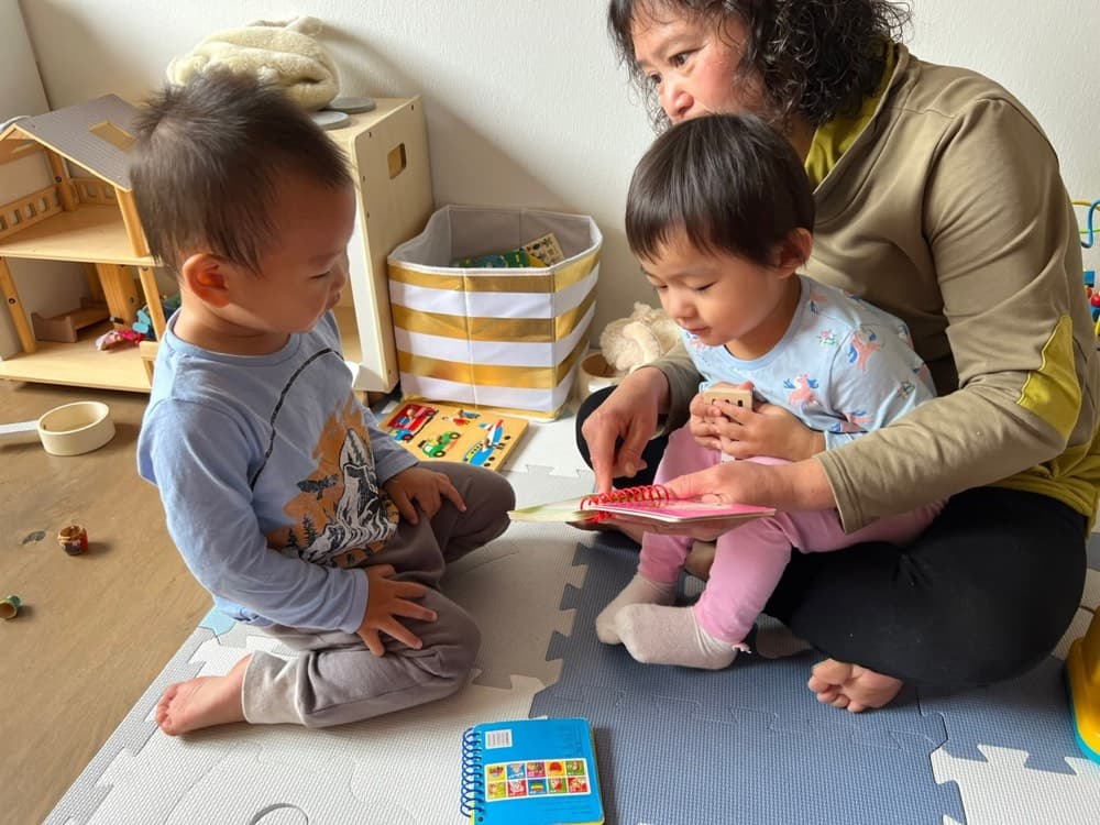 Caregiver reading with two toddlers during indoor play