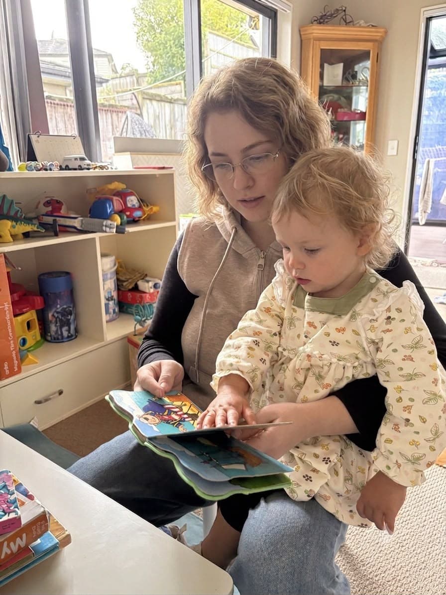 Nanny reading a picture book with a toddler on her lap