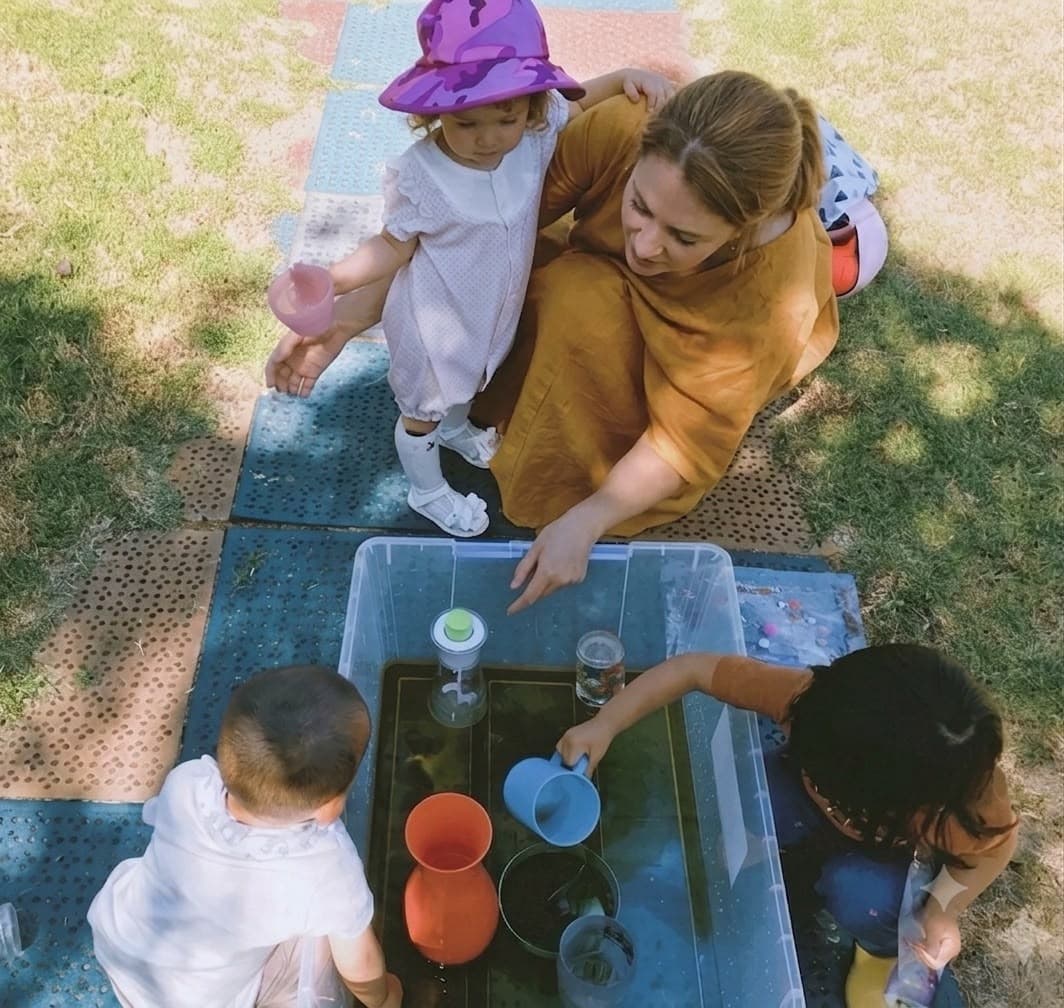 Nanny leading a sensory water-play activity with young children