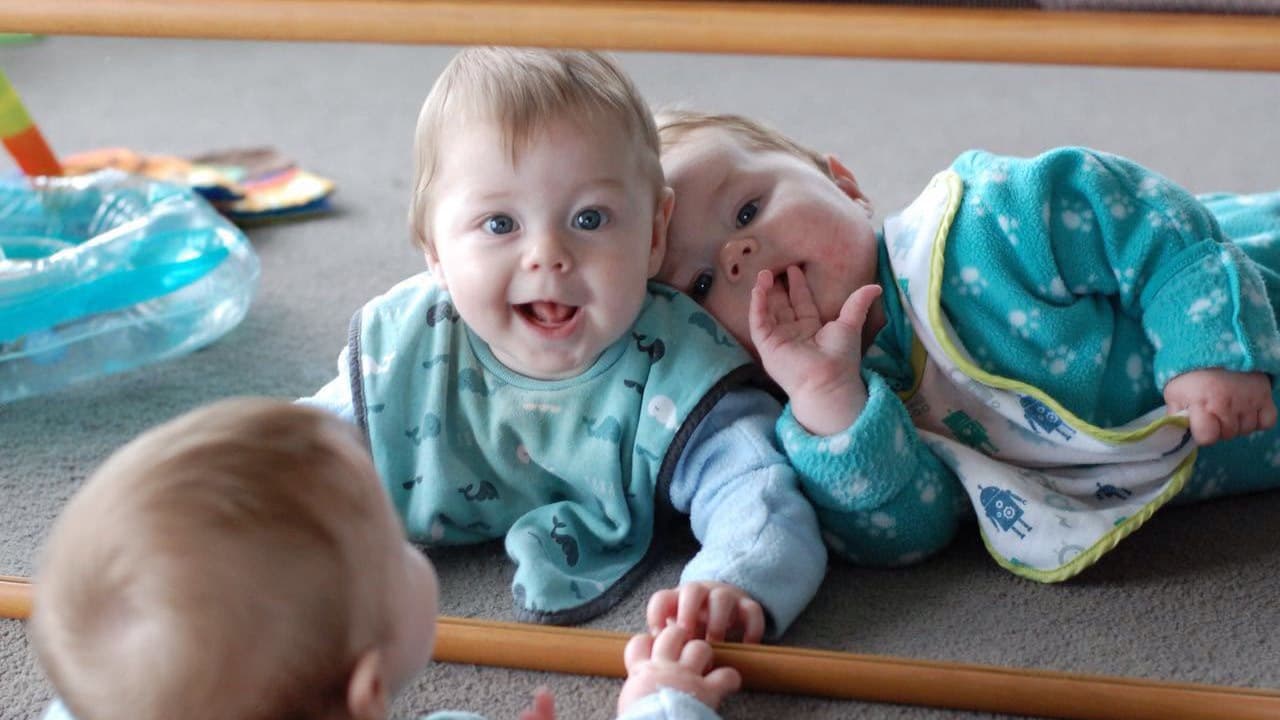 Babies playing happily in front of a mirror during home-based care