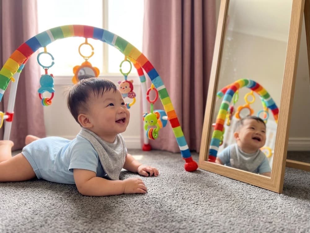 Infant exploring a mirror beside a play gym